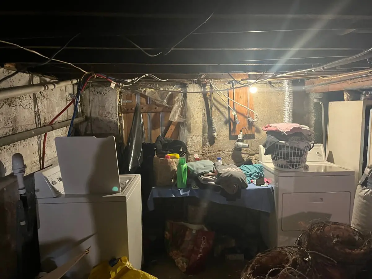 Selling a house in a flood zone in Islip: dim unfinished basement crowded with laundry and stored items