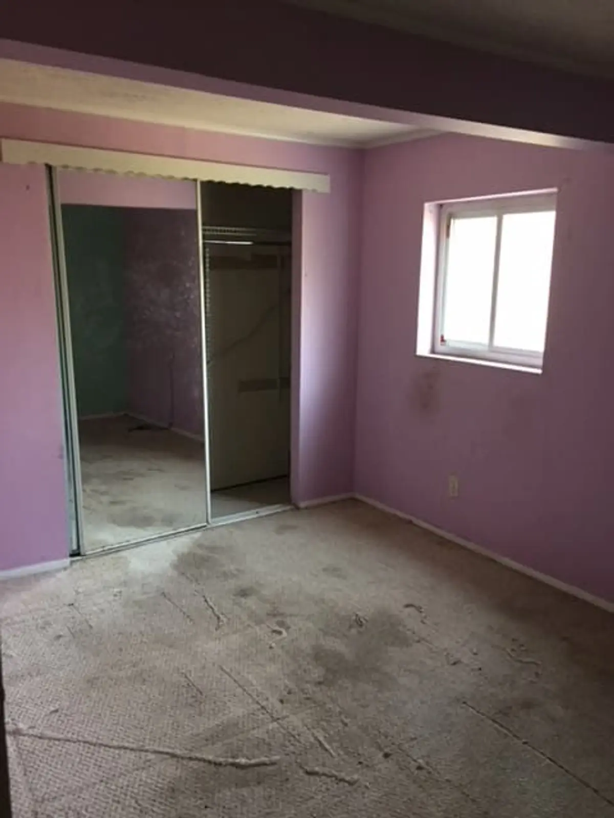 Selling a parent’s house after a move to care in Islip: empty purple bedroom with stained carpet and mirrored closet doors
